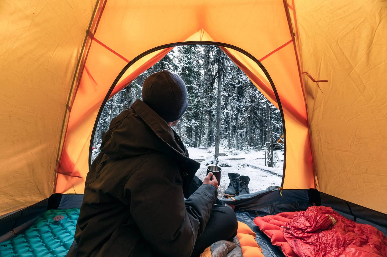 A person sitting inside a tent in the snow, finding solace and peace in the serene winter landscape.