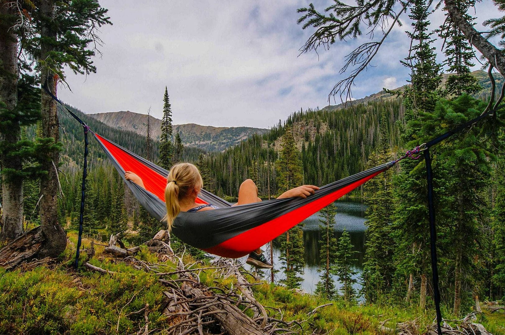 Enjoy a virtual tour of a woman peacefully laying in a hammock near a serene lake within the stunning views of a campground.