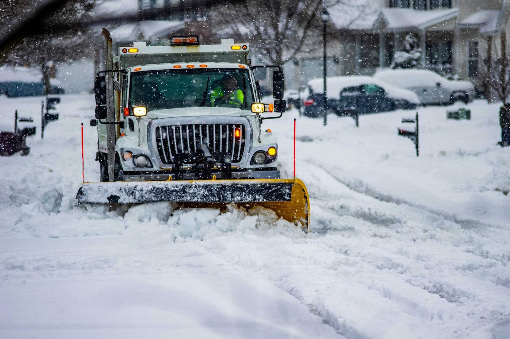 A snow plow driving down a Goshen residential street, clearing accumulated snow.