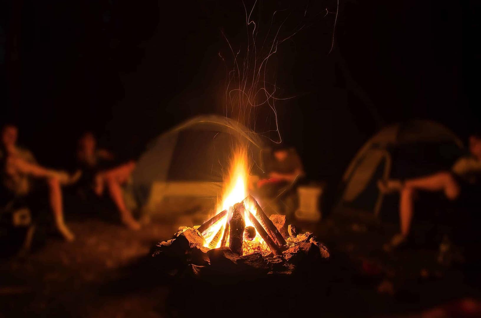 A group of people sitting around a campfire at night, enjoying the safety and warmth provided by the campground.
