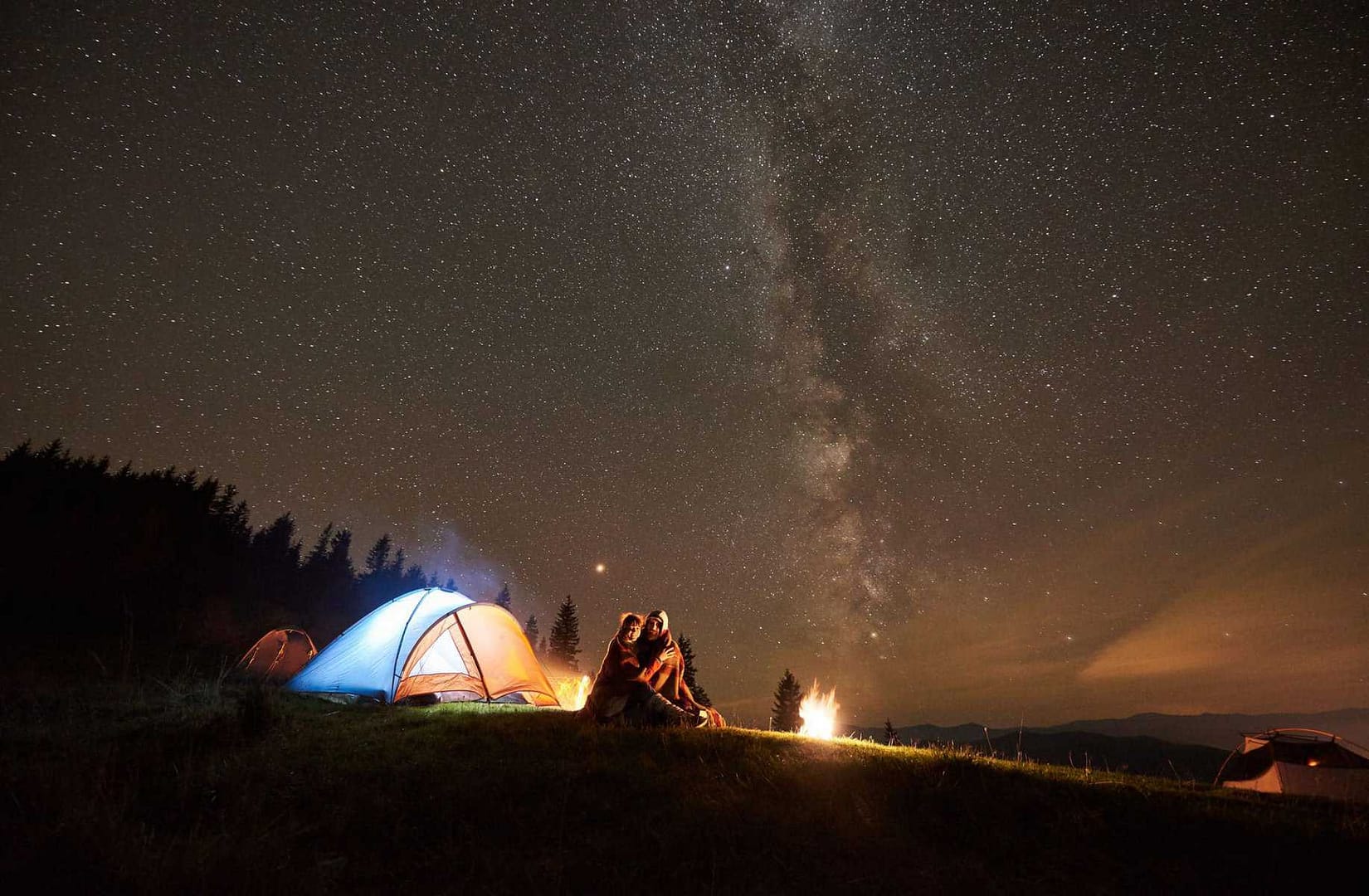 A couple sits around a campfire under a starry sky in a Dark Sky Park.