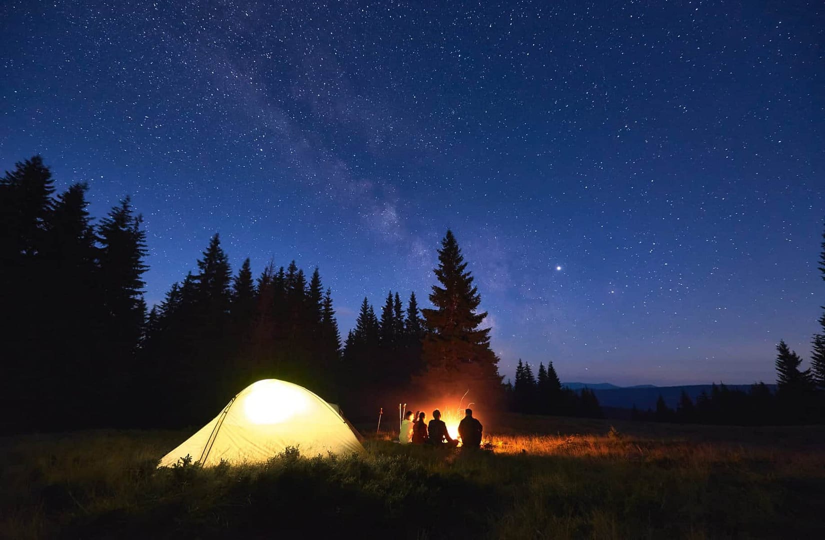 Two people sitting around a campfire at night, abiding by the Responsible Camping Bylaw.