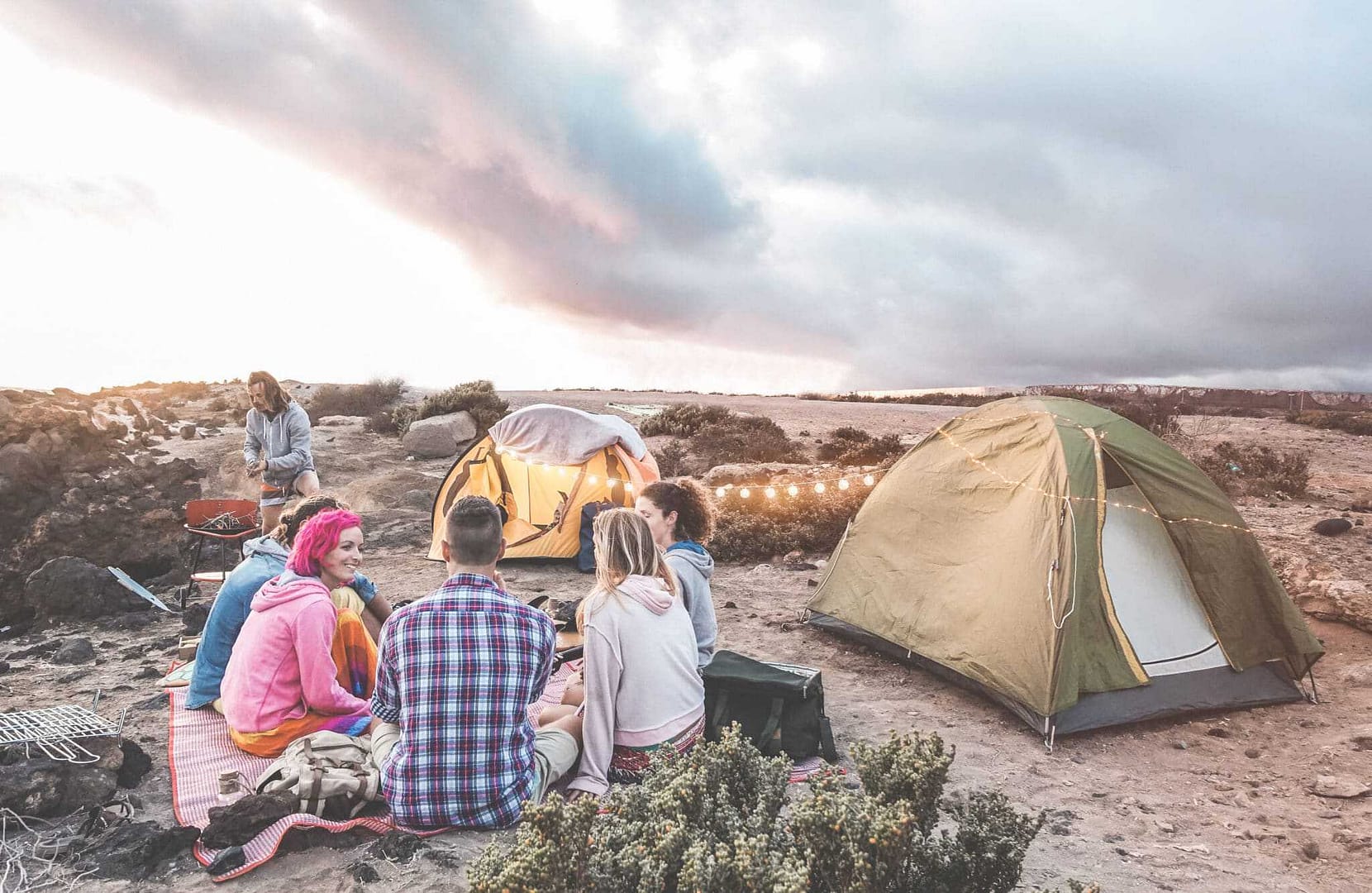 A group of people caravanning in Western Australia, sitting around a tent in the desert.
