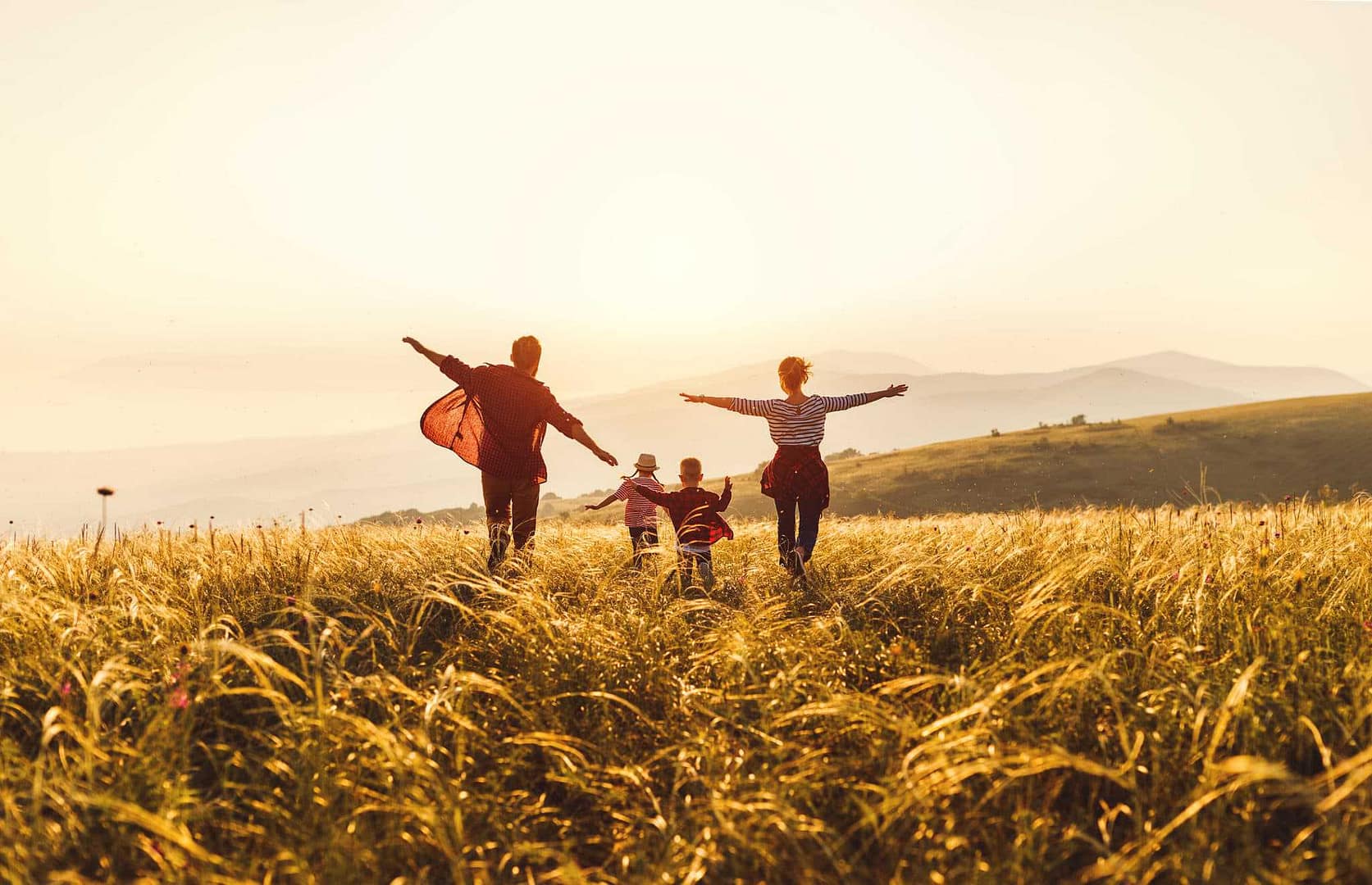 A family is enjoying a pleasant evening, sprinting and laughing while playing in an open field at sunset.