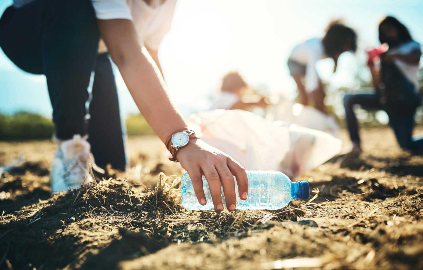 A local woman is picking up a plastic bottle in the dirt.
