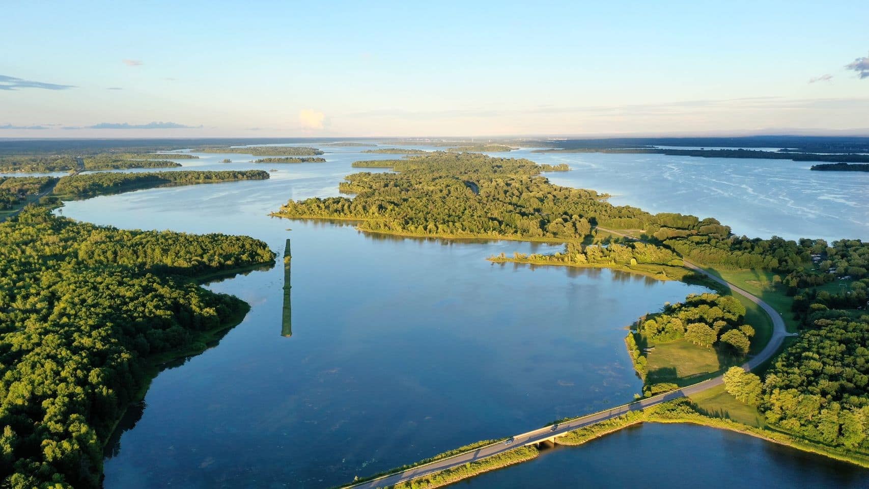 Aerial view of a tranquil lake with surrounding greenery and a road running along its shore at sunset, near the historic St. Lawrence Parks.