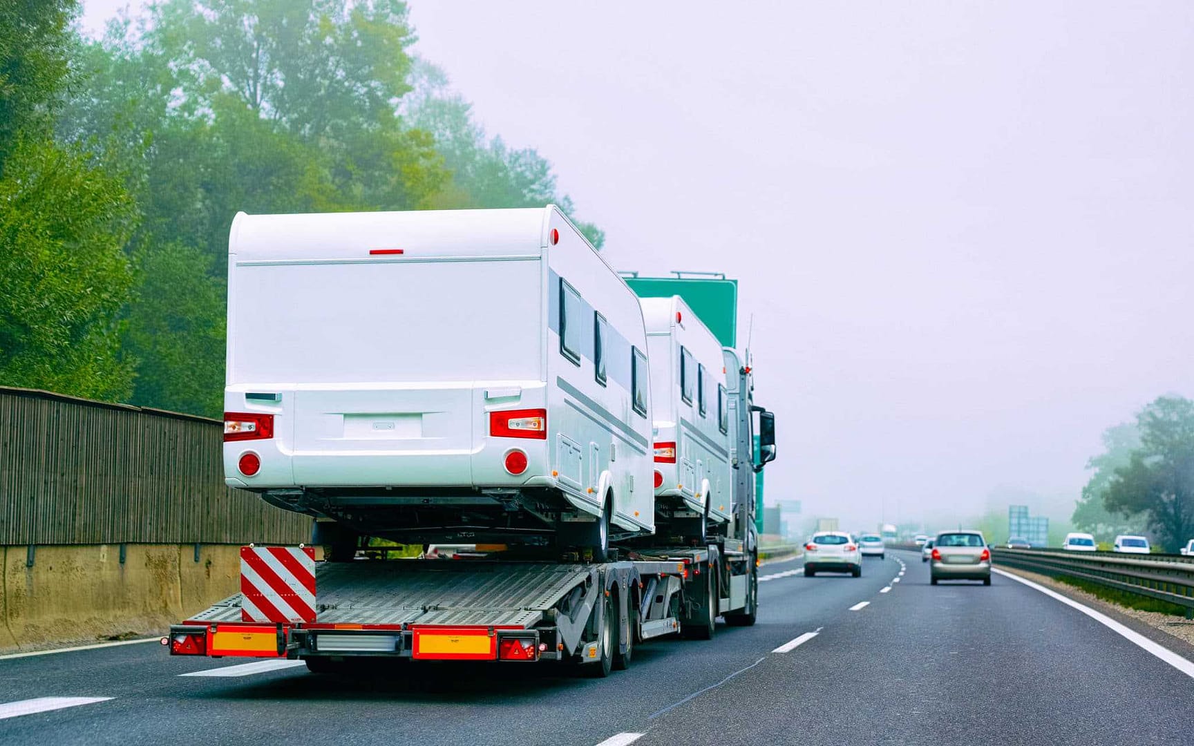A white RV on a flatbed truck on a highway, featured on the Canadian RV Buy & Sell Marketplace.