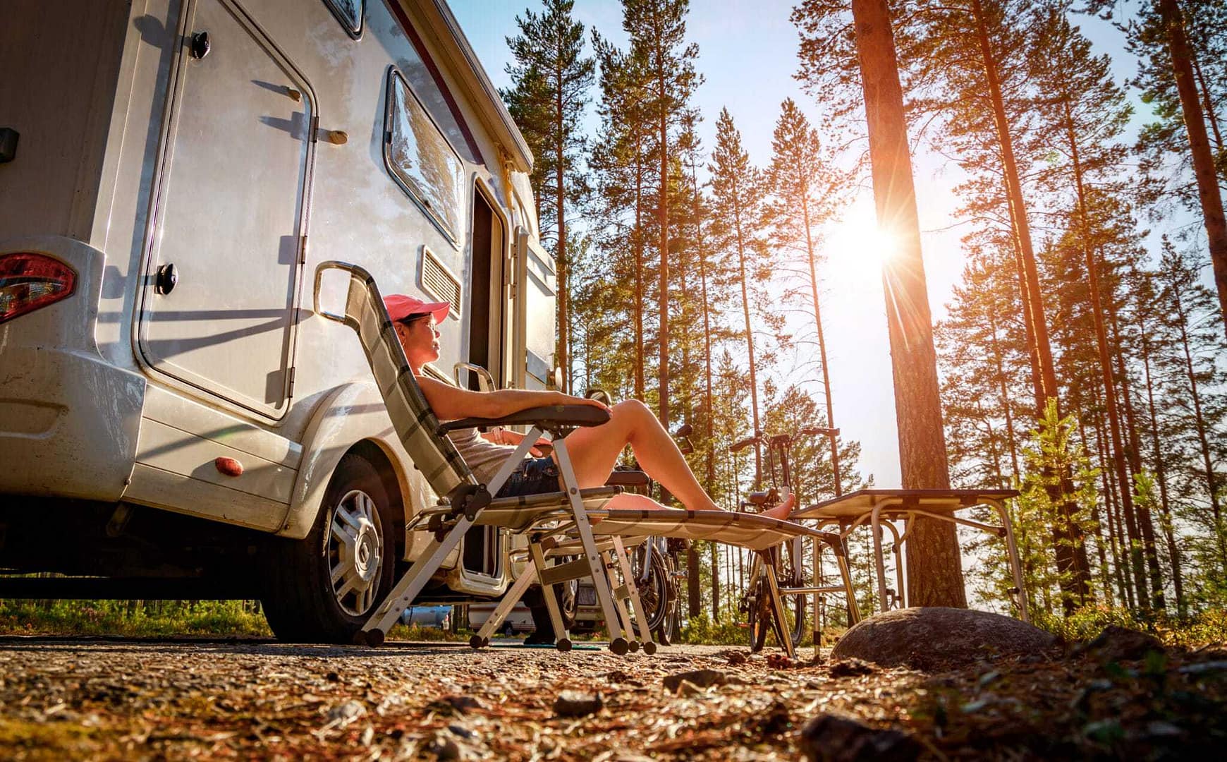 A woman sits in a camper van next to an RV in the woods.