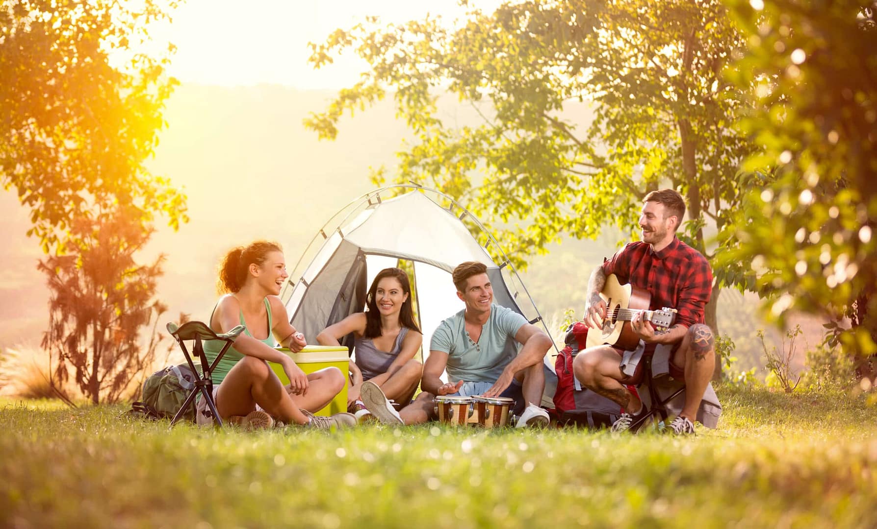 Four friends enjoying a camping trip near a tent, with one playing a guitar, in a grassy area during an auto draft.