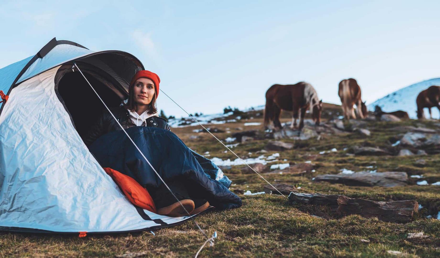 A woman sits in a rustic tent with horses in the background at a local equestrian campground.