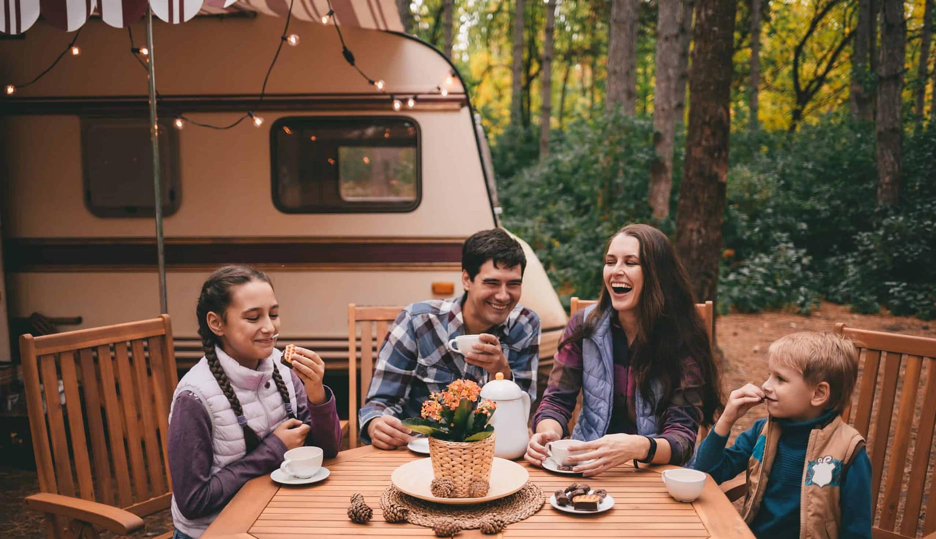 A family sits at a table in front of an RV, enjoying their vacation.