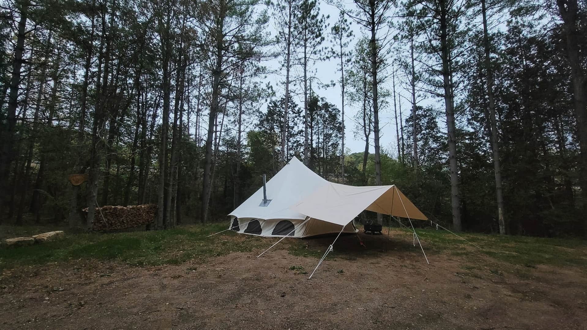 Embracing Nature amidst the Aefintyr Campground, a white tent stands gracefully in the middle of a wooded area.