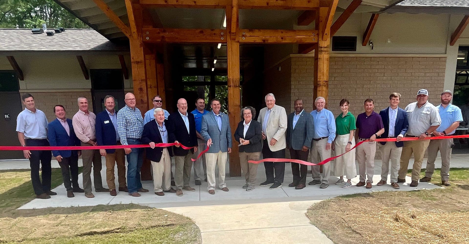 A group of people stands in front of a building at a ribbon-cutting ceremony, holding scissors poised to cut the red ribbon. With a red mat on the ground, it almost feels like an Auto Draft moment in its precise synchronization and celebratory spirit.