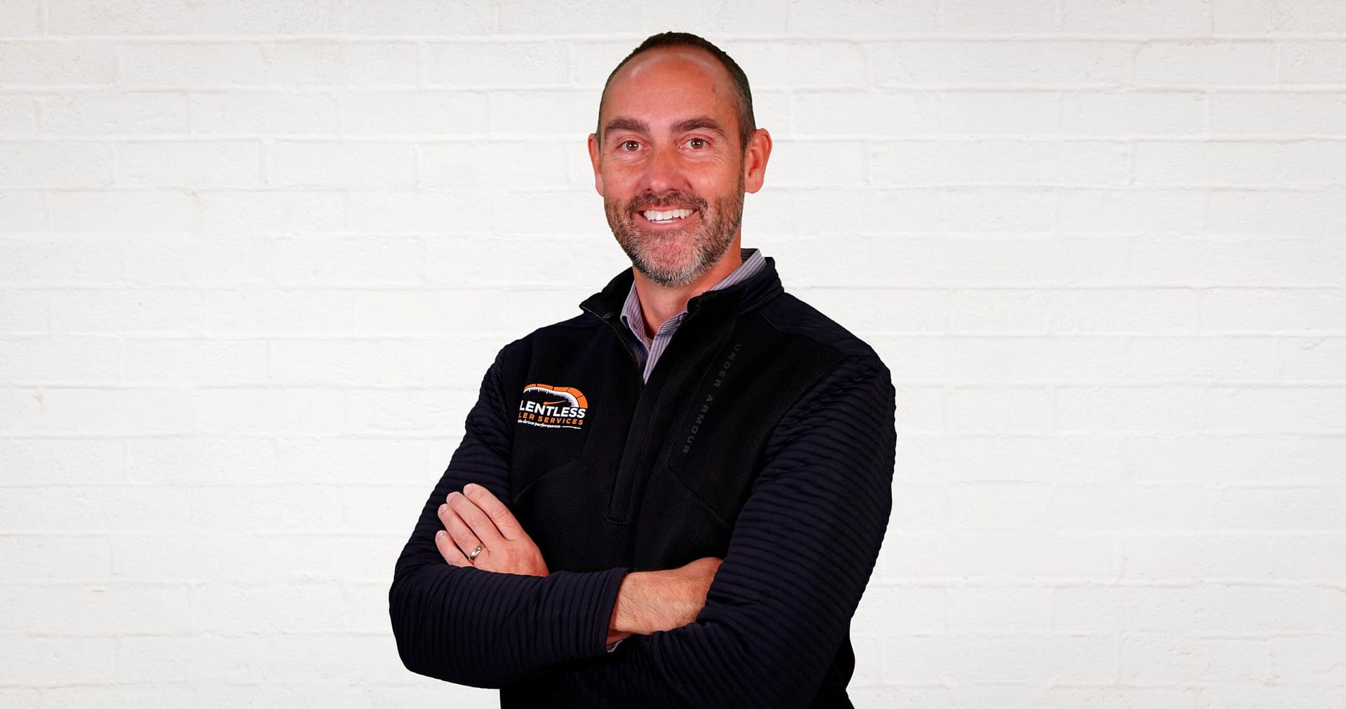 A finance specialist attending the RV Dealers Convention/Expo, standing with his arms crossed in front of a white brick wall.