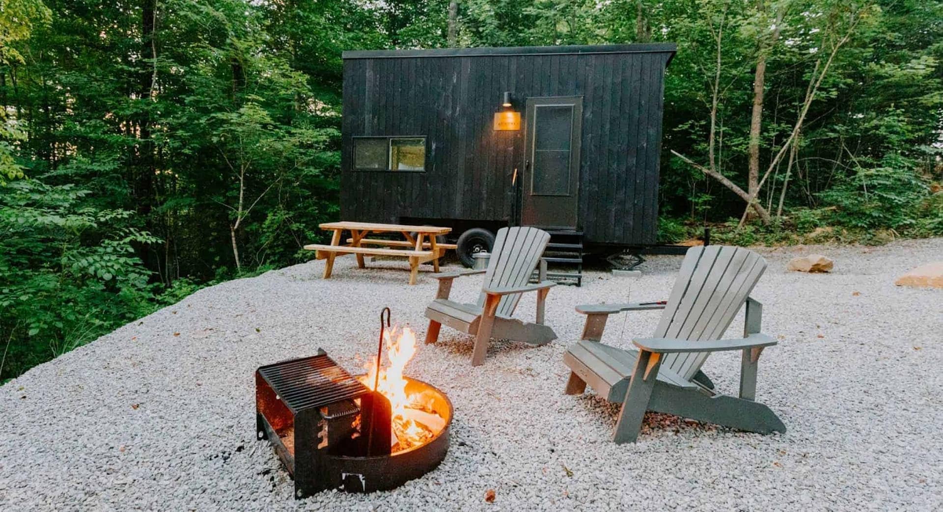 A Brooklyn-Based tiny house sits next to a fire pit in the woods.