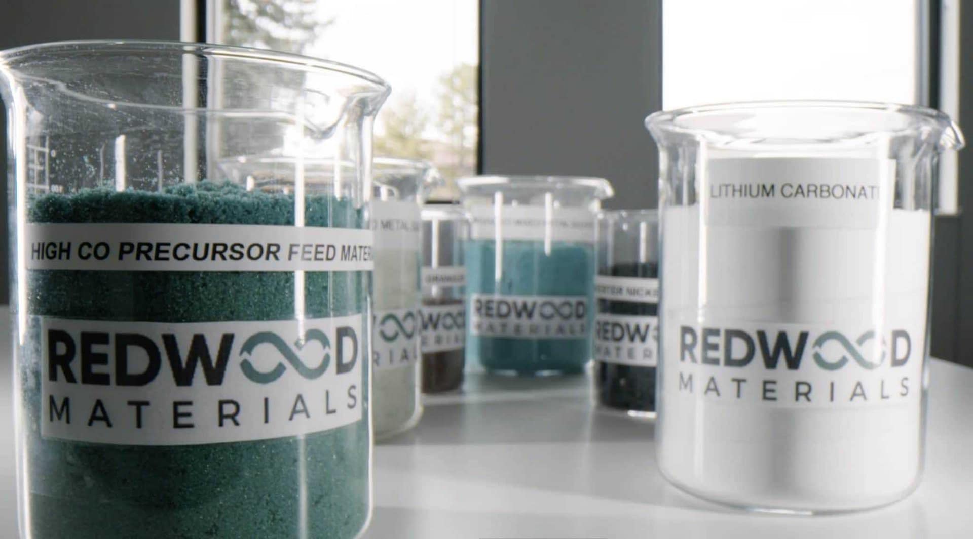 A beaker containing Redwood Materials sits on the table, showcasing their closed-loop battery recycling process. This sustainability initiative aligns with Ford's commitment to eco-friendly practices.