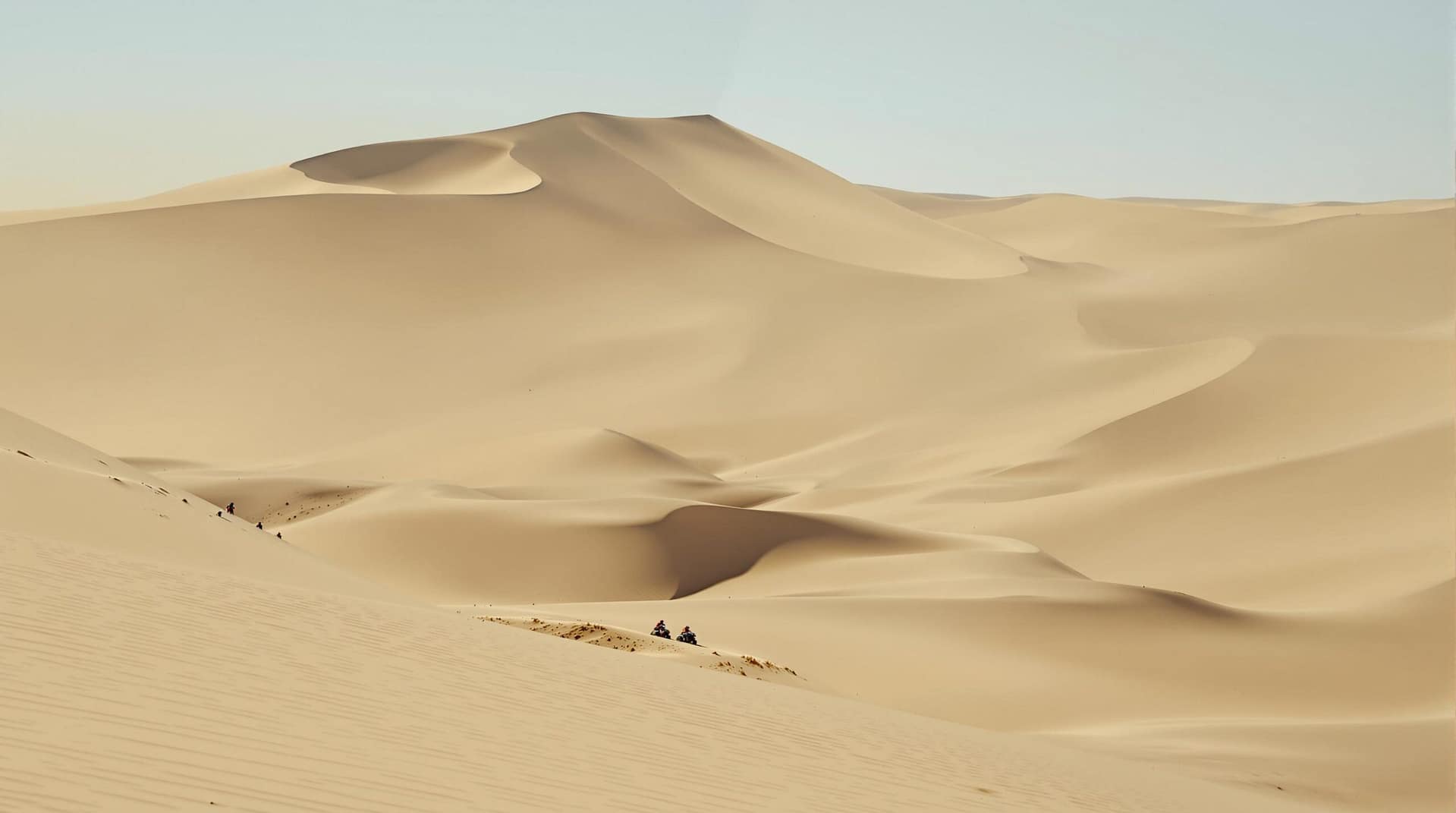 Wide sand dunes under a clear sky with off-road riders in helmets, showcasing the steep terrain and emphasizing safety precautions.