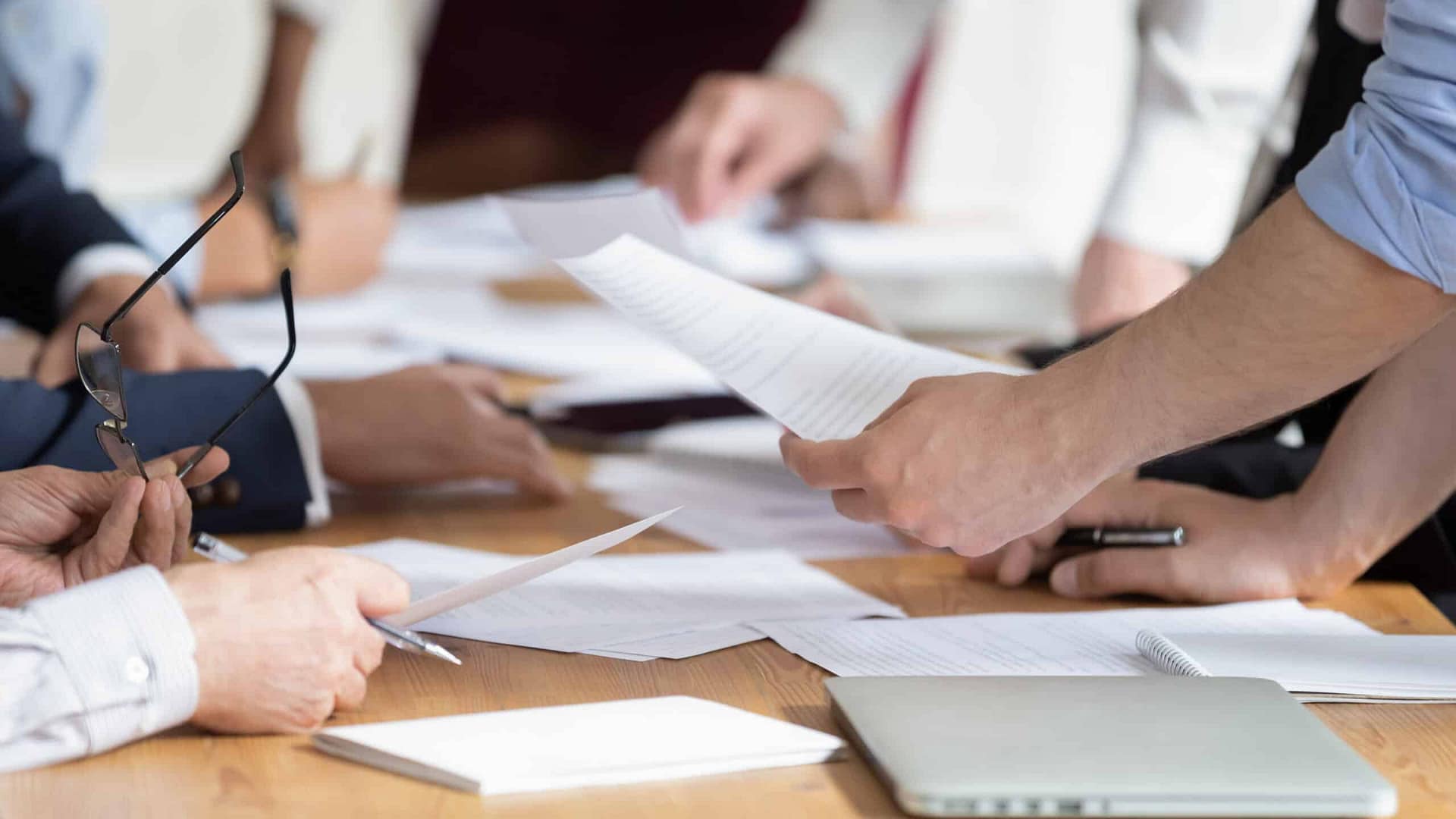 A business meeting in progress with a closeup of participants' hands exchanging auto draft documents over a table.