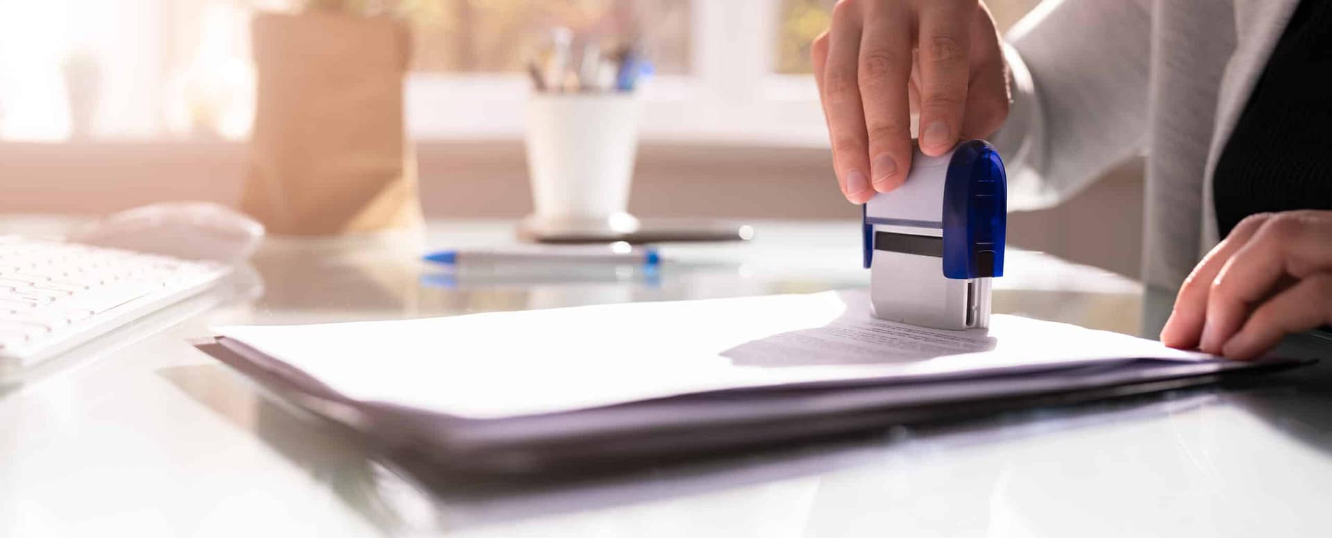 A person is using a stamp to mark a stack of documents on a glass desk, readying them for final approval. Office stationery, including a pen and computer keyboard, are visible in the background—an efficient scene likely tied to the Planning Commission's review of an RV Park proposal.