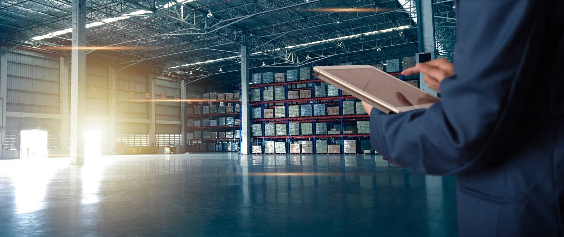 A man in a suit is holding a tablet in a warehouse, portraying an identity crisis within the US manufacturing industry.