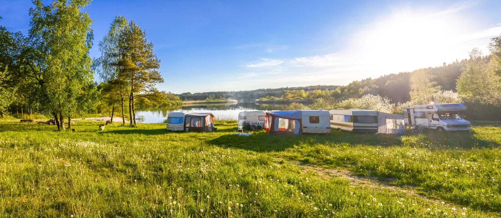 A collection of RVs parked in a grassy area near a lake, perfect for campgrounds & RV parks.