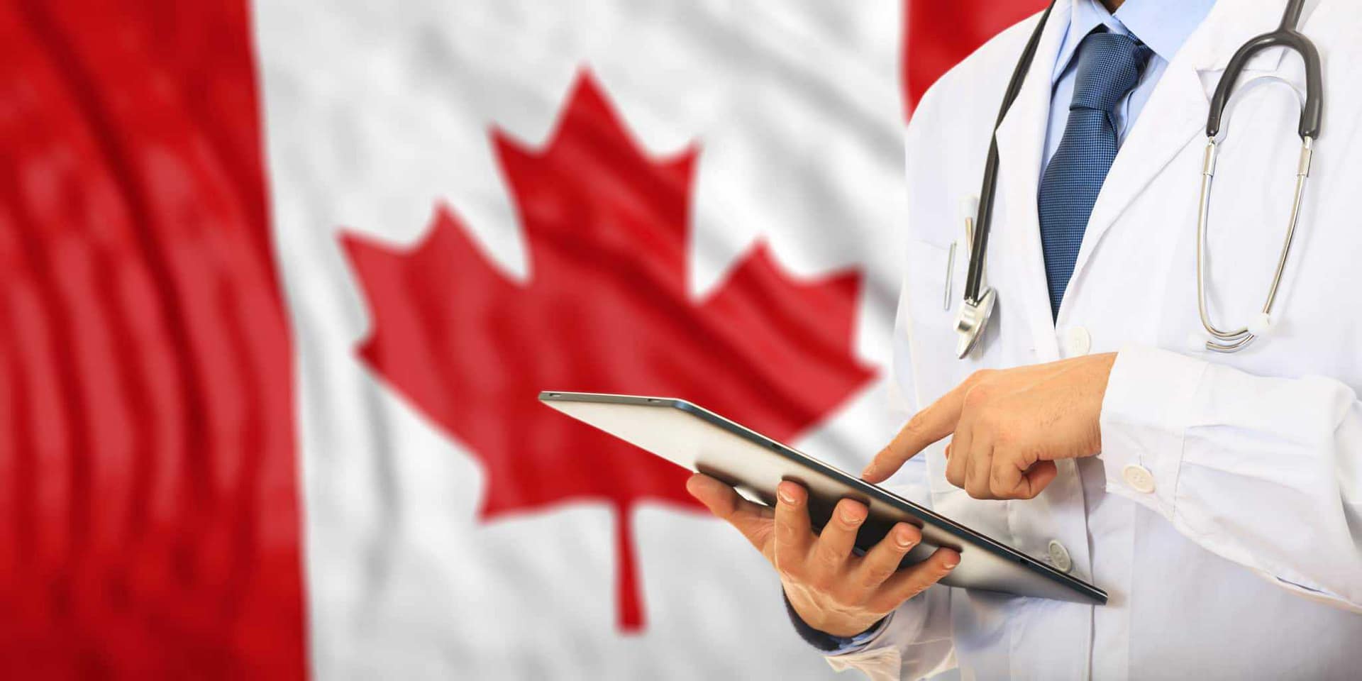 A doctor holding a tablet in front of a Canadian flag in Manitoba.