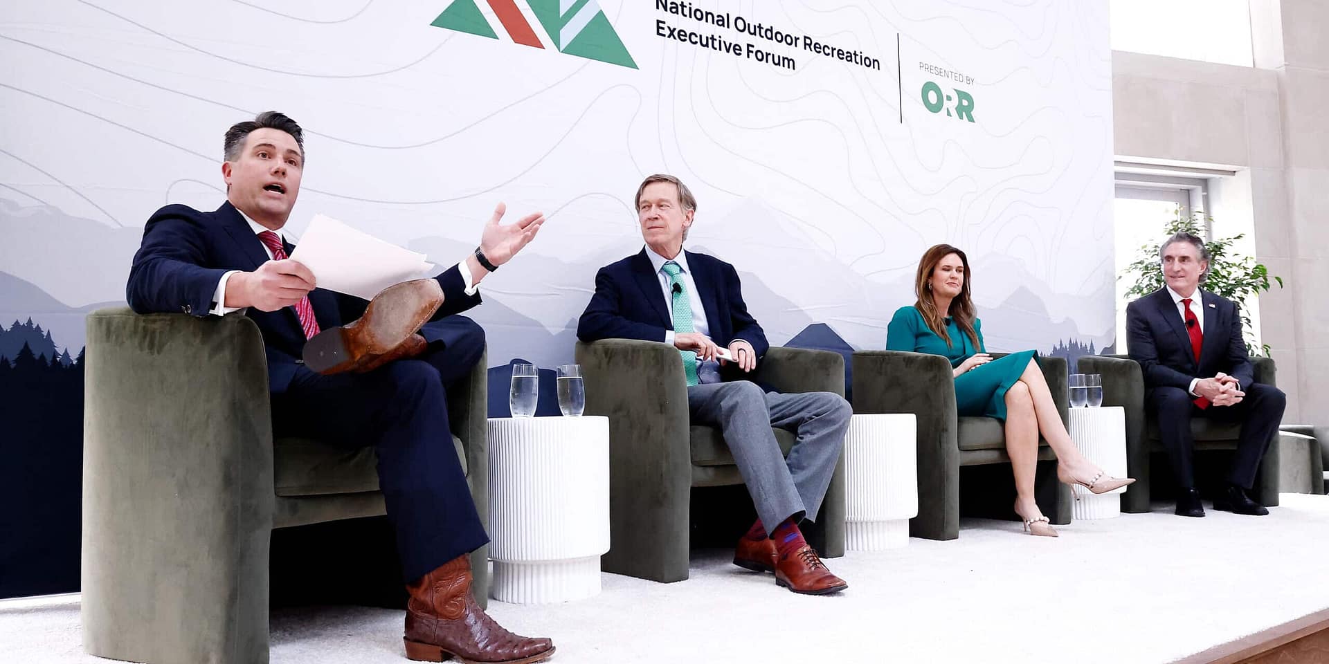 Four panelists are discussing at a national outdoor recreation executive forum, seated on white stools against a backdrop with forest imagery, focusing on auto draft and SEO keywords.