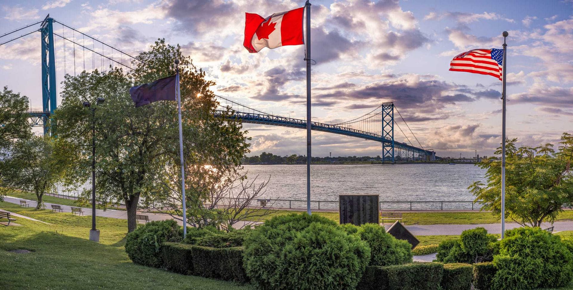 Two flags flying in front of a bridge, symbolizing the looser border restrictions between Canada businesses.