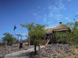 An African hut with a thatched roof in the middle of a grassy area, offering a unique glamping experience for your bucket list.