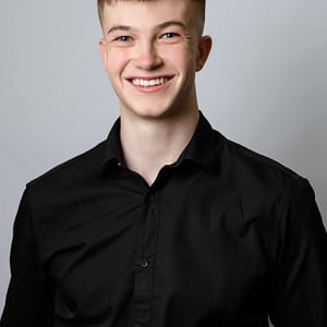 A young man smiling in a black shirt while participating in MC Fireside Chats.