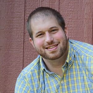 A man smiling in front of a wooden wall during the MC Fireside Chats on December 21st, 2022.
