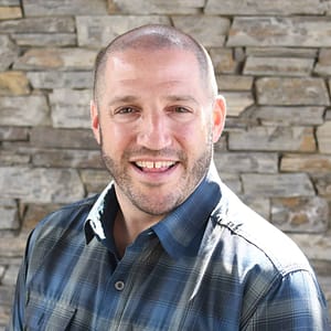 On December 21st, 2022, a man in a plaid shirt is smiling in front of a stone wall during an MC Fireside Chat.