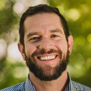 MC Fireside Chats: A bearded man enthusiastically smiling in front of trees while hosting a fireside chat, scheduled for December 14th, 2022.