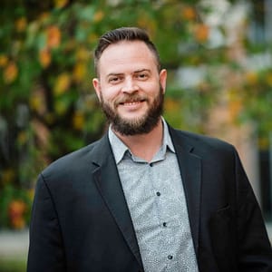 A man with a beard smiling in front of a tree during the MC Fireside Chats on December 14th, 2022.