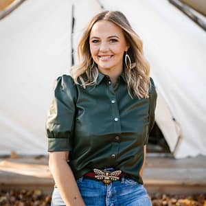 A woman in jeans and a leather shirt is posing in front of a tent during MC Fireside Chats on June 14th, 2023.