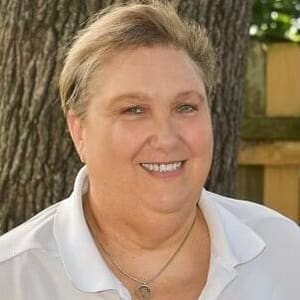 A woman in a white shirt smiling in front of a tree during MC Fireside Chats on August 16th.