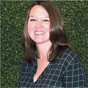 A woman smiling in front of a green wall during MC Fireside Chats.