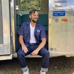 On September 27th, 2023, a man indulges in MC Fireside Chats while comfortably seated in the door of an airstream trailer.