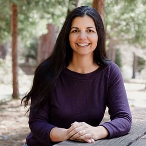 A woman sitting on a picnic table in the woods during MC Fireside Chats, October 18th, 2023.