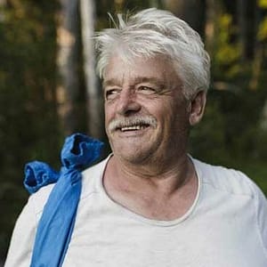 An older man smiling in the woods during MC Fireside Chats.