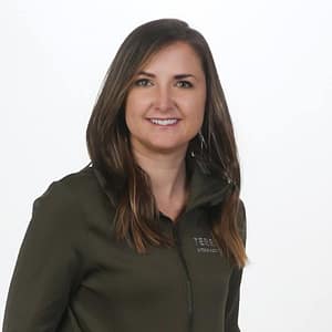 A woman in a green jacket smiles in front of a white background during the January 31st episode of MC Fireside Chats.