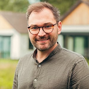 A man in glasses smiling in front of a house during an MC Fireside Chats event.