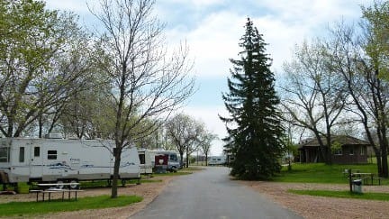The River Park Campground in Weyburn offers a tranquil setting with parked RVs nestled among lush trees. Experience the beauty of nature while enjoying the comfort and convenience of a well-maint
