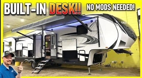 A man is standing in front of a Grand Design Reflection RV with a built-in office desk.