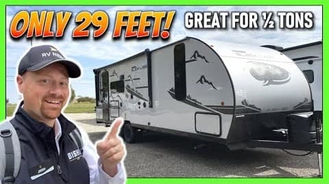 A man is posing in front of a Cherokee Grey Wolf Travel Trailer.