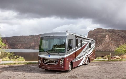An Holiday Rambler rv parked in front of a lake with mountains in the background.