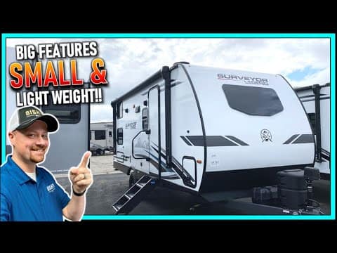 A man is pointing at a small and light weight travel trailer by Forest River.