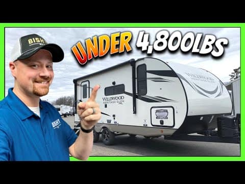 A man is pointing to a lightweight Heritage Glen travel trailer.