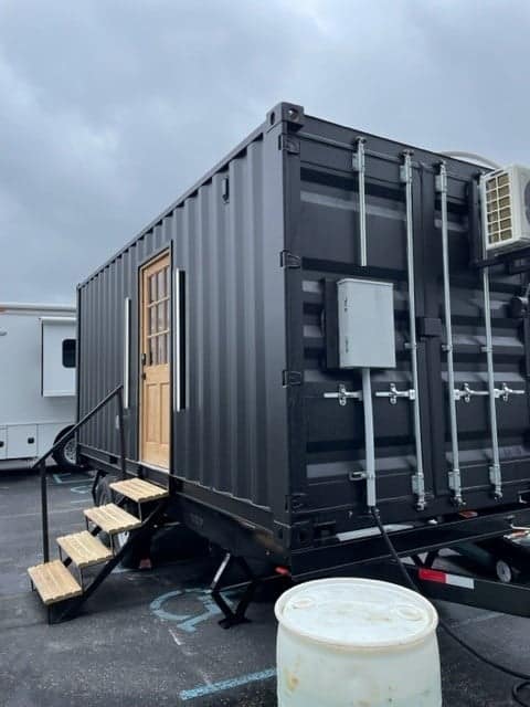 An eco-friendly black shipping container, designed by Ekō Solutions, is parked in a parking lot.