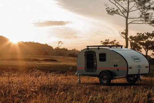 A teardrop camper parked in a field at sunset, displaying at the Let's Go Caravan and Camping Show.